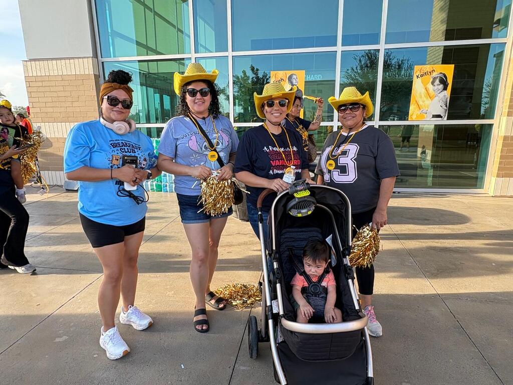 Group of women, some wearing cowboy hats, with a baby in a stroller, standing outside a glass building.