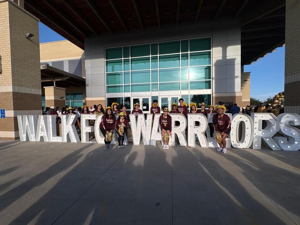 A group stands in front of large letters spelling "WALKER WARRIORS" on the ground, in front of a building.