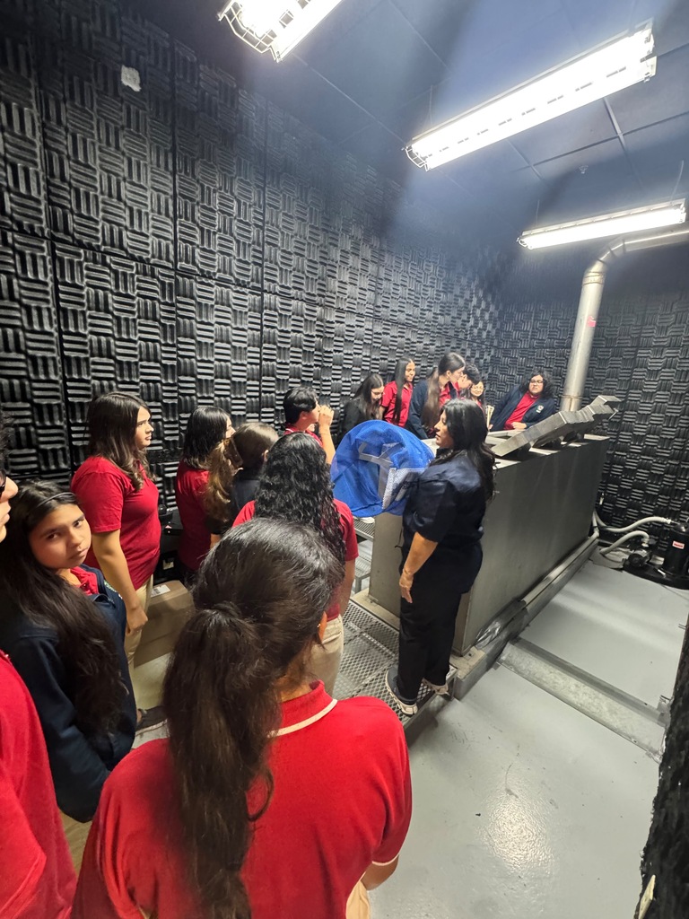 Several people in red shirts are indoors, possibly in a training facility. They are gathered near a metal structure.