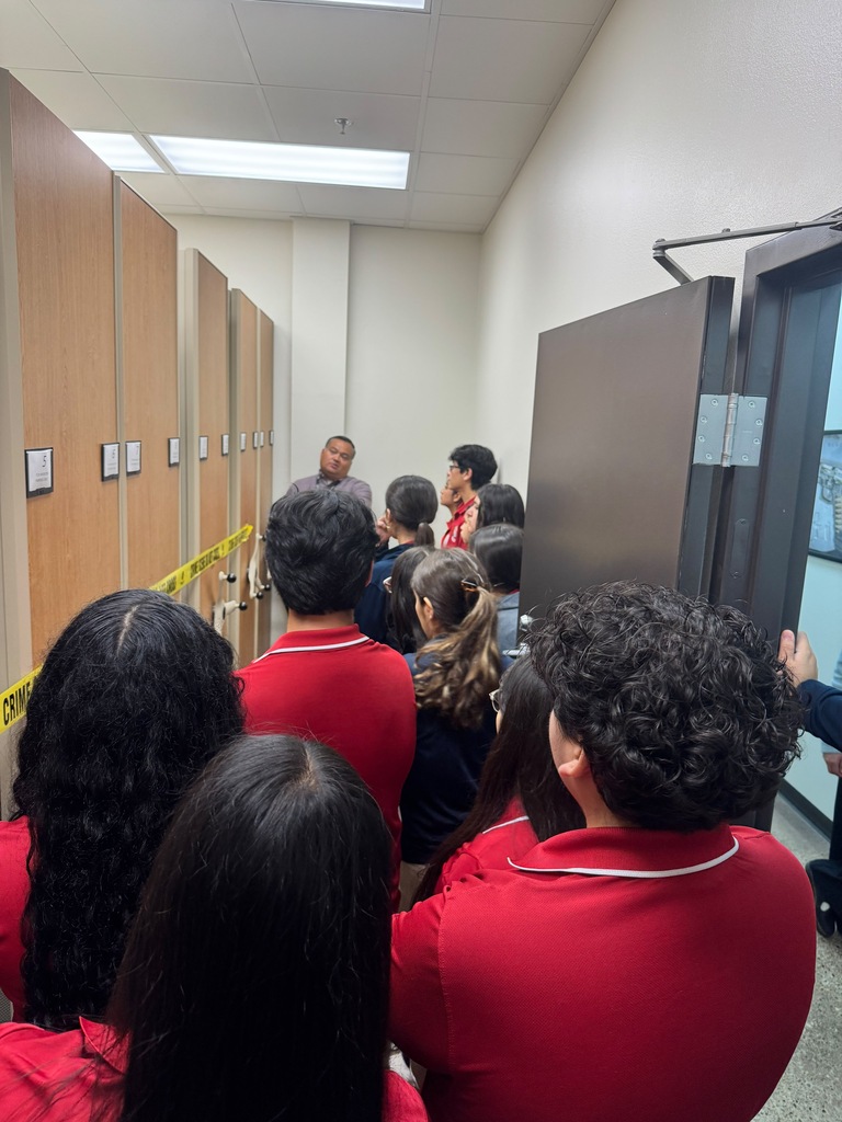 People in red shirts gather around a man at a school, some facing a locker room.