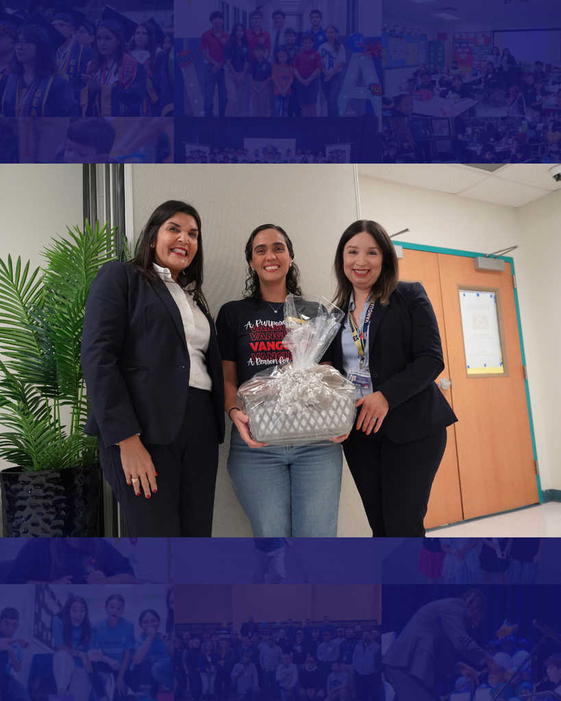 Three women in business attire stand next to each other, one holding a large gift. Behind them is a door and a plant.