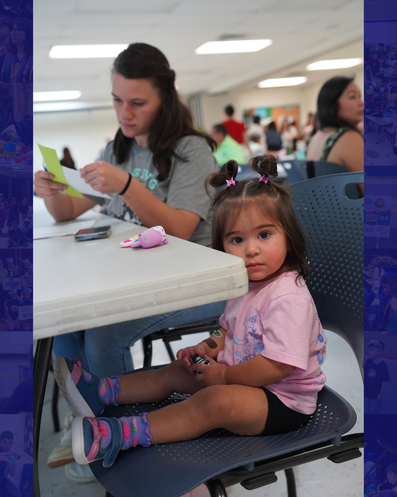 A woman sits at a table with a young girl in front of her. The girl wears a pink shirt and colorful shoes.