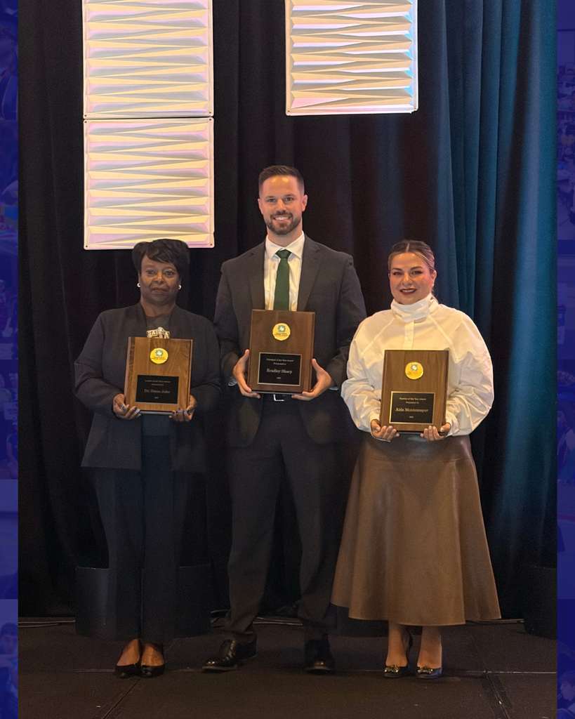 Three people standing on stage in formal attire holding awards, blue curtains in the background.