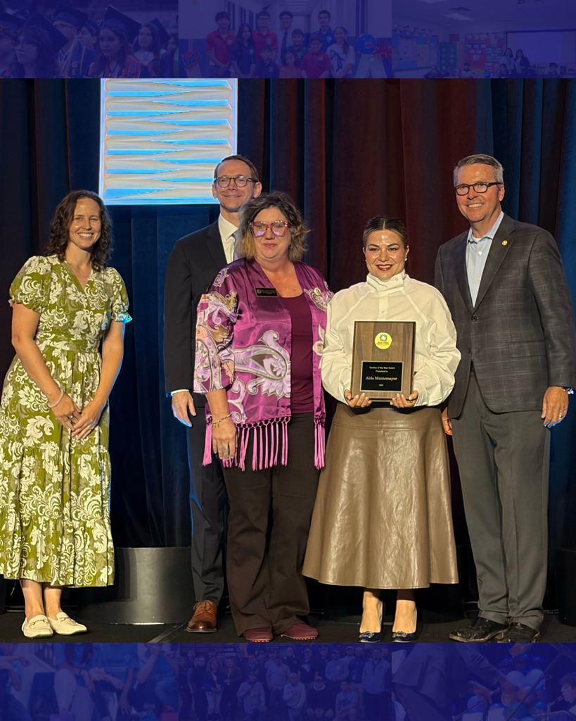 Five people stand on stage, with one in the center holding an award plaque. The woman on the left wears a green dress.