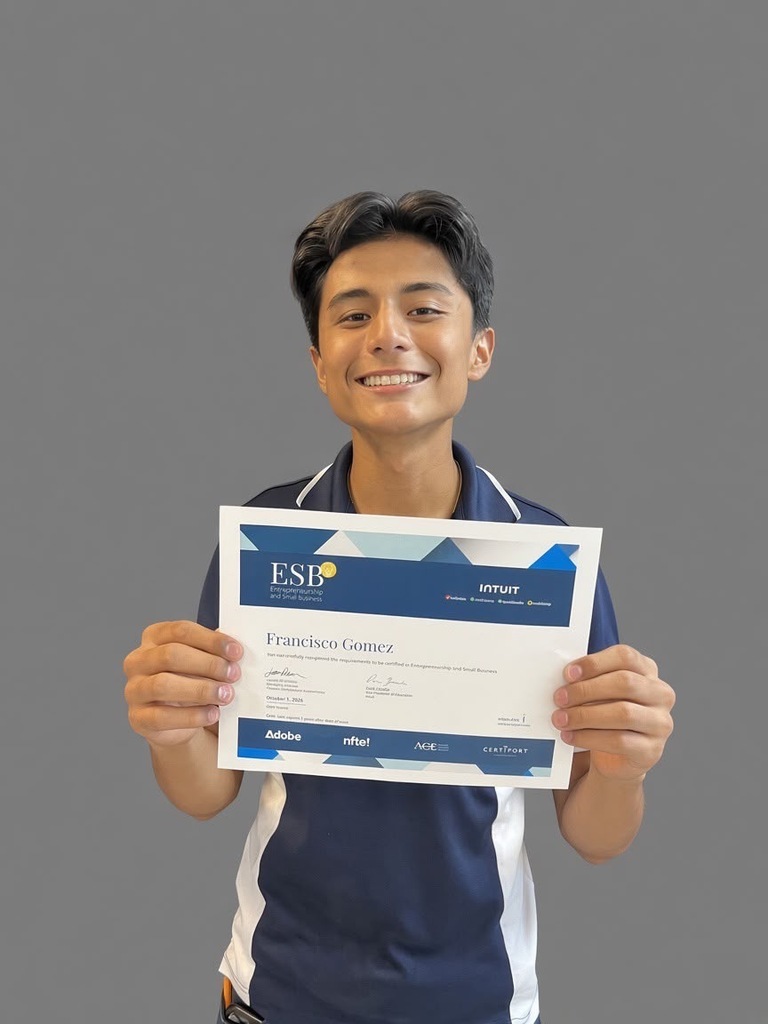Person in navy blue and white polo holding a certificate with text "ESB" and "Francisco Gomez" in front of a gray background.