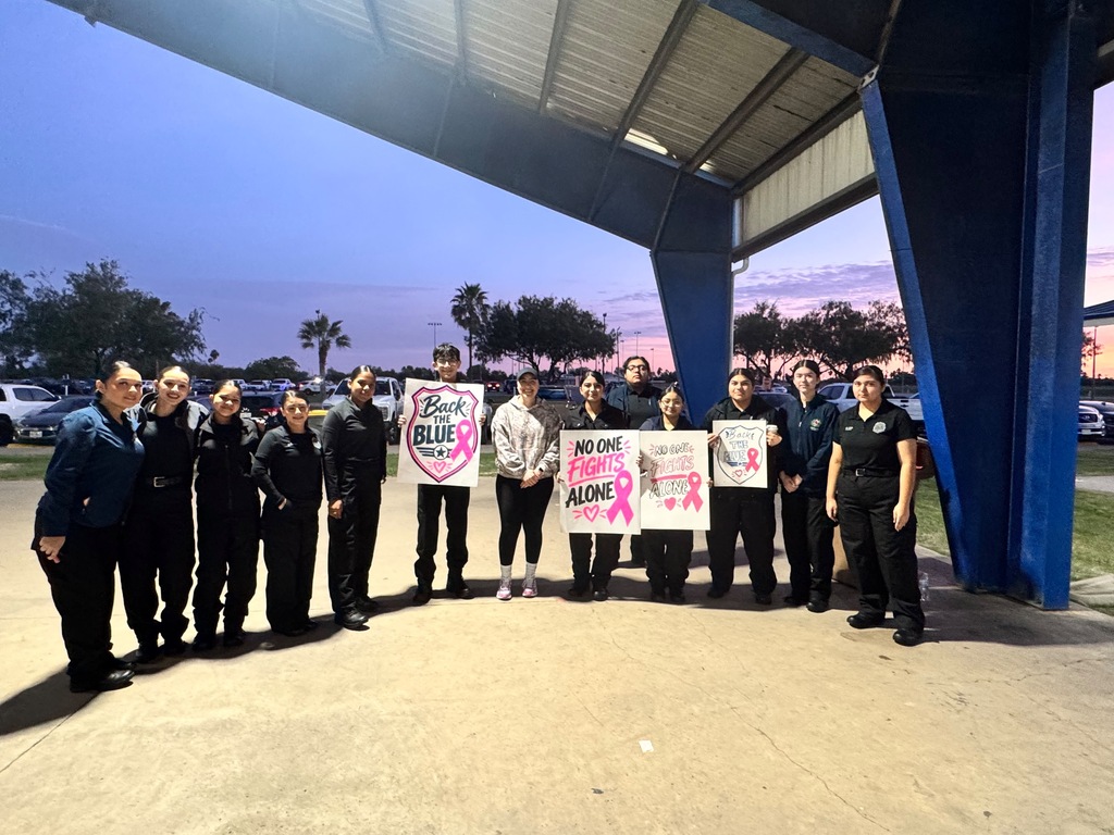 Group of adults in uniform holding signs with pink and white text under an overhang.