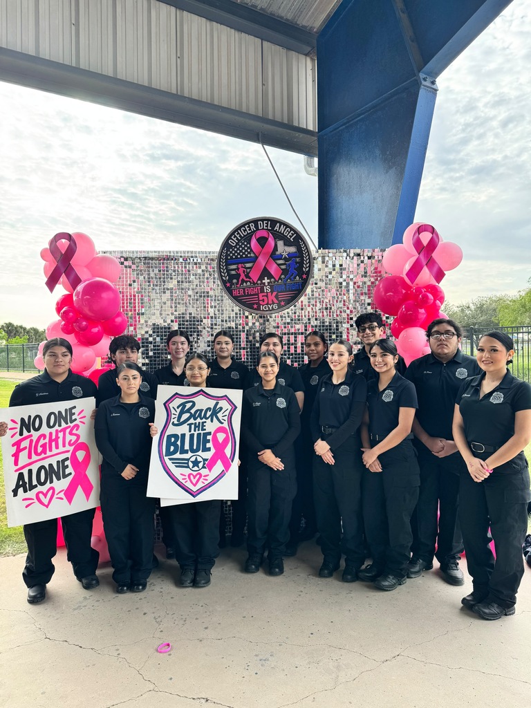 Group of students and staff wearing black uniforms with pink heart balloons and signs behind them.