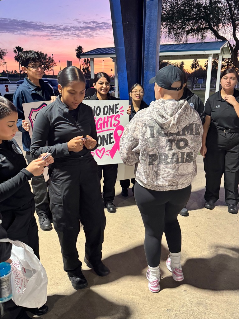 A group of students outside, holding signs. One sign reads "No One Fights Alone". Students wear athletic clothing and sneakers.