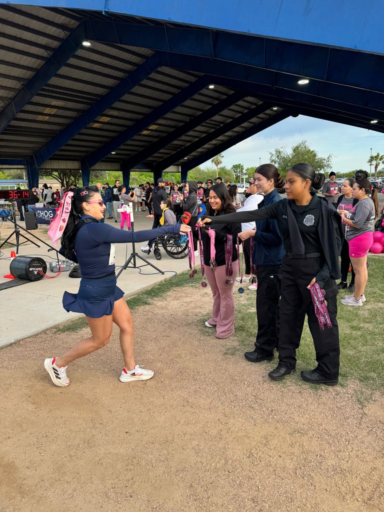 Students in uniform and shoes running on a dirt track, with others standing in a shelter.
