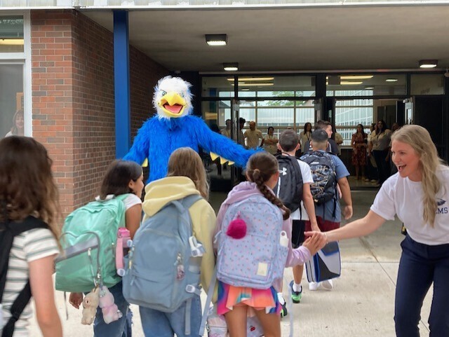 Students arriving to school being greeted by the principal and mascot