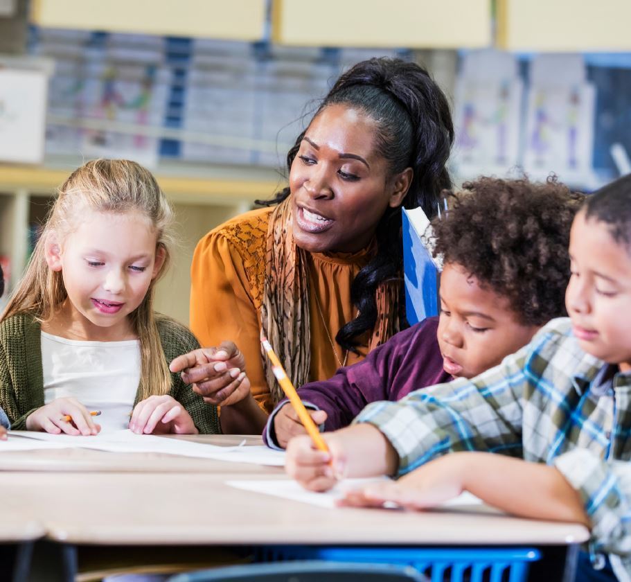 Teacher sitting at desk engaging in a lesson with 3 students