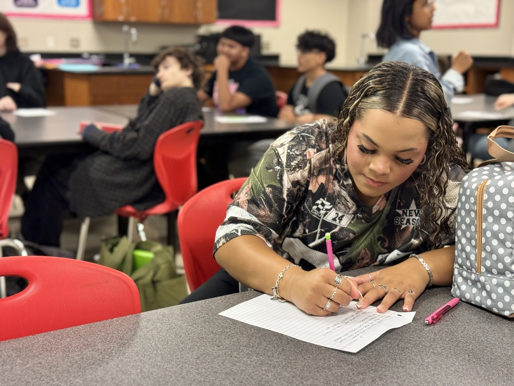 girl at school desk writing on paper with pencil