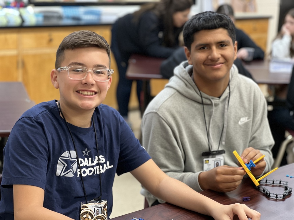 two students at a desk smiling at camera
