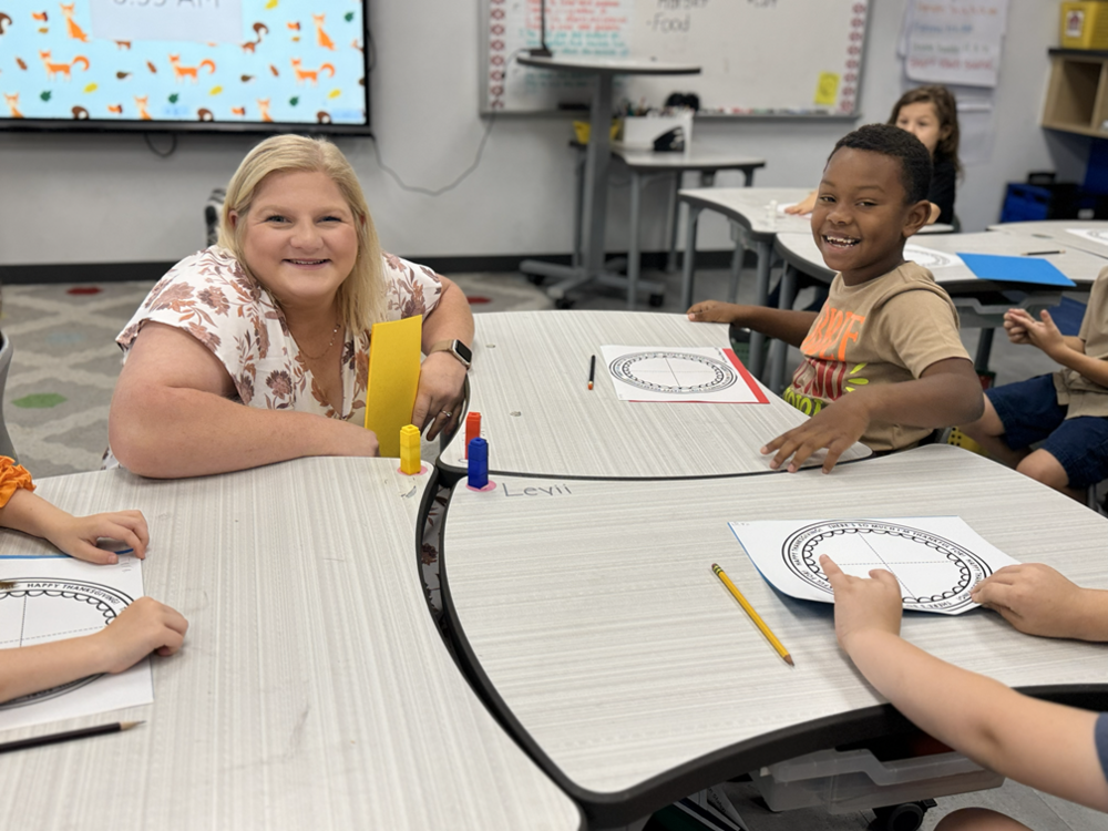 teacher and student smiling at desk in classroom