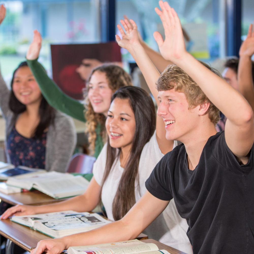 High School students smiling and raising hands in class