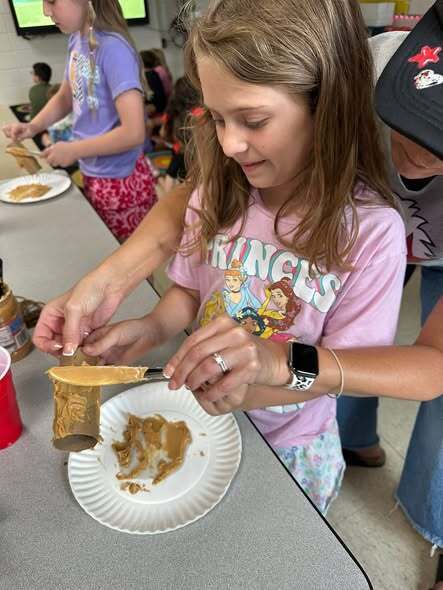 Student putting peanut butter on cardboard tube.