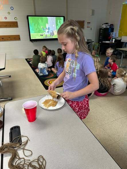 Student putting peanut butter on cardboard tube.