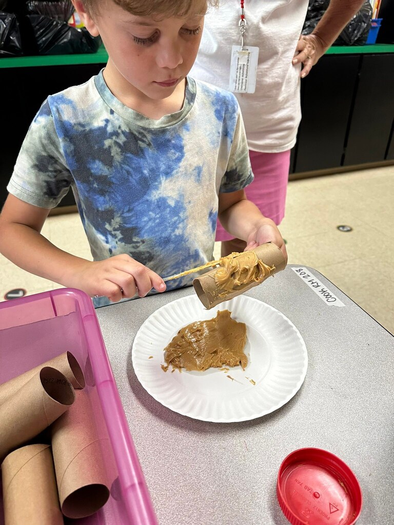 Student putting peanut butter on cardboard tube.