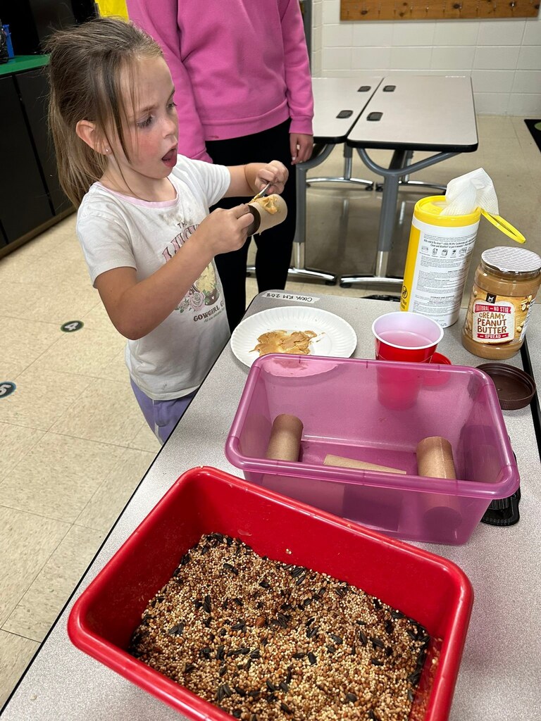 Student putting peanut butter on cardboard tube.