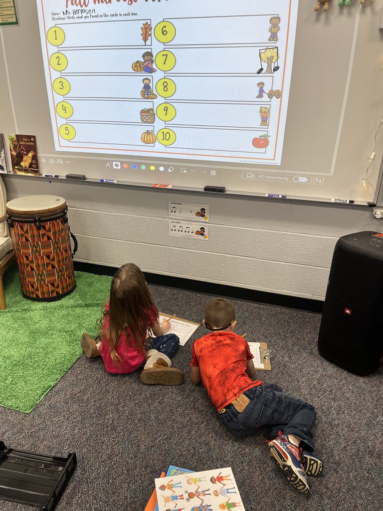 Students kneeling on the ground in front of the whiteboard with clipboards.