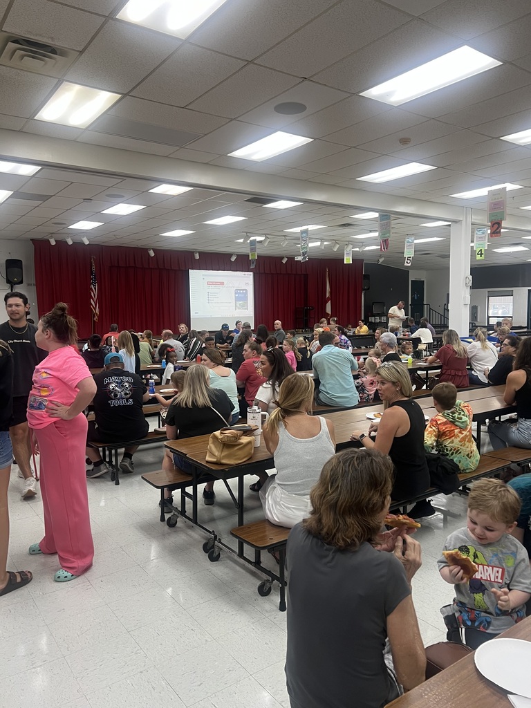 Families in the cafeteria eating pizza.