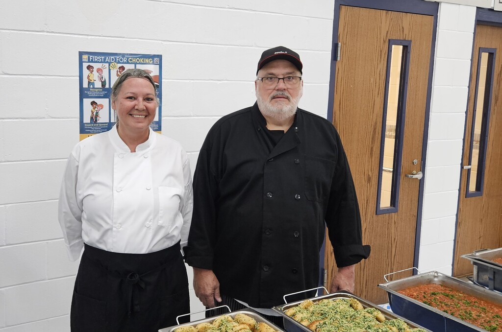Two Wakulla County Schools Food Services staff members stand beside trays of food prepared for the War Eagle Football team.