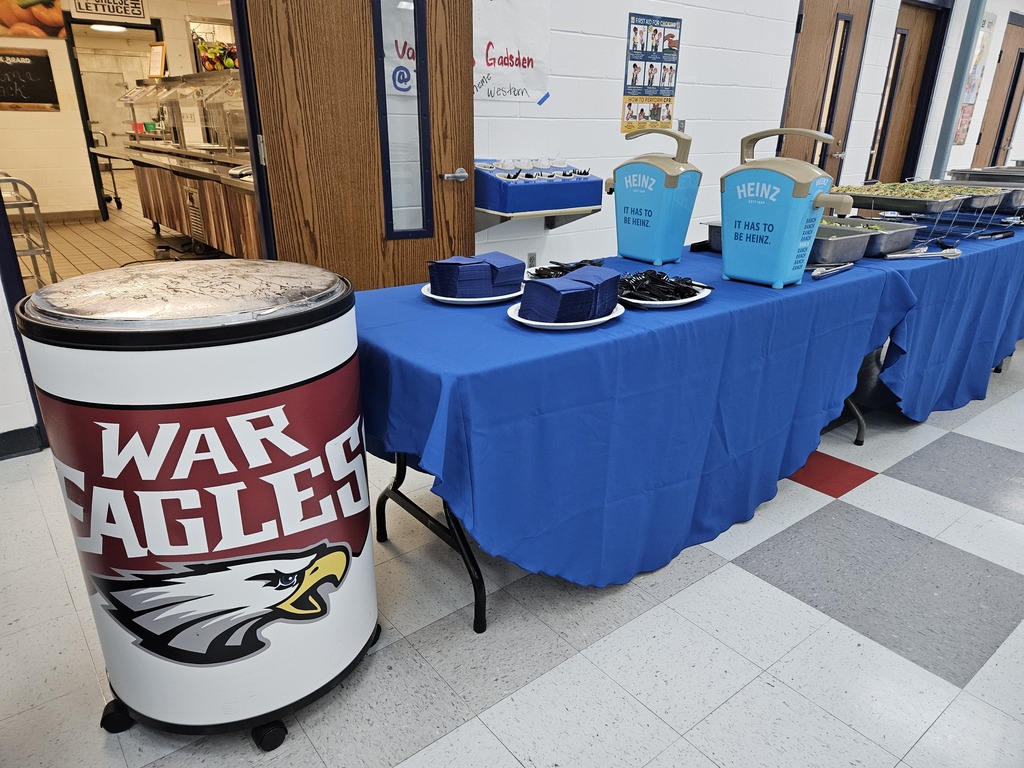 Food Services meal setup with serving tables, condiments and trays of food beside a War Eagles container.