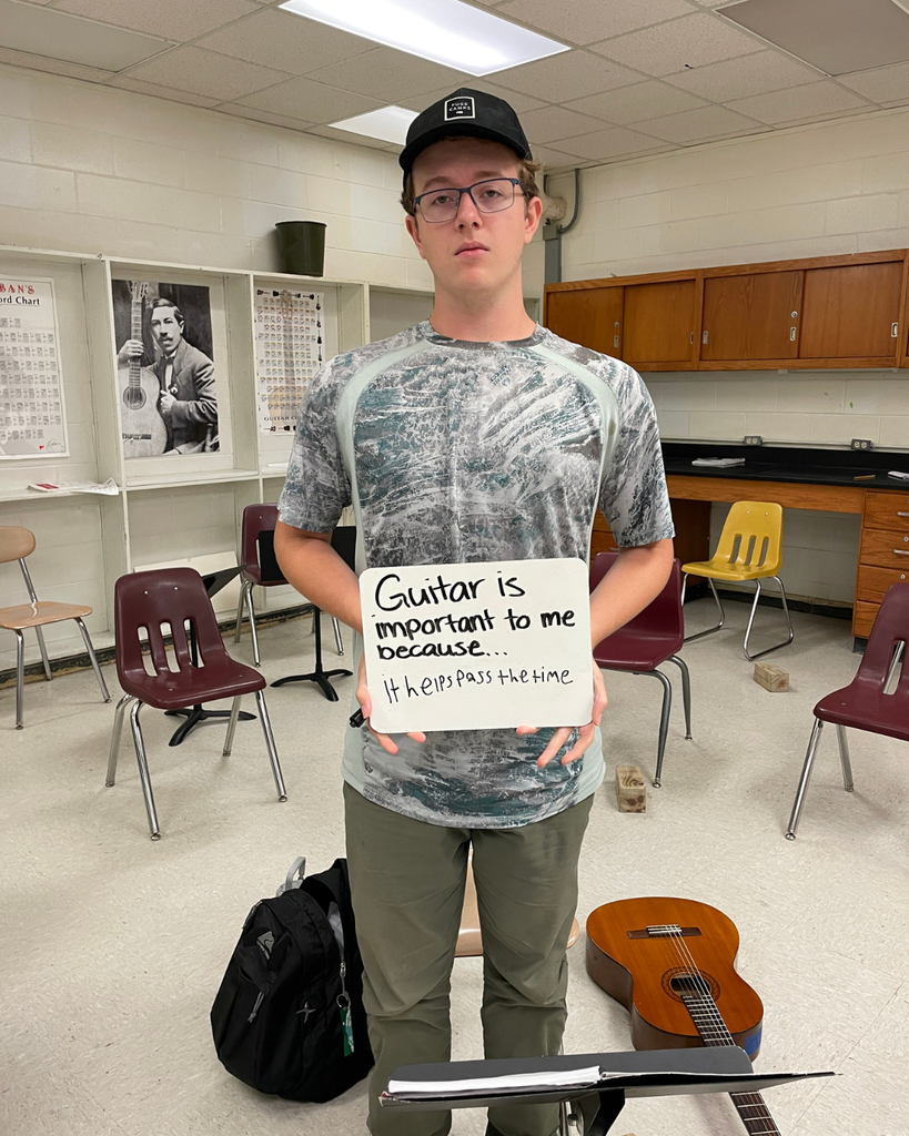 The image pictures a student with a sign that says,"Guitar is important to me because... it helps pass the time"