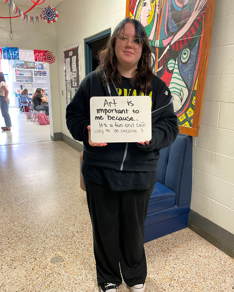 The image pictures a student with a sign that says,"Art is important to me because... it's a fun and safe way to be creative"