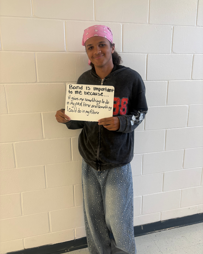 A student holding a sign saying,"Band is important to me because...it gives me something to do in my past time and something I could do in my future "