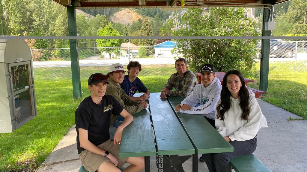 Shop students and teacher sitting at picnic table they made.