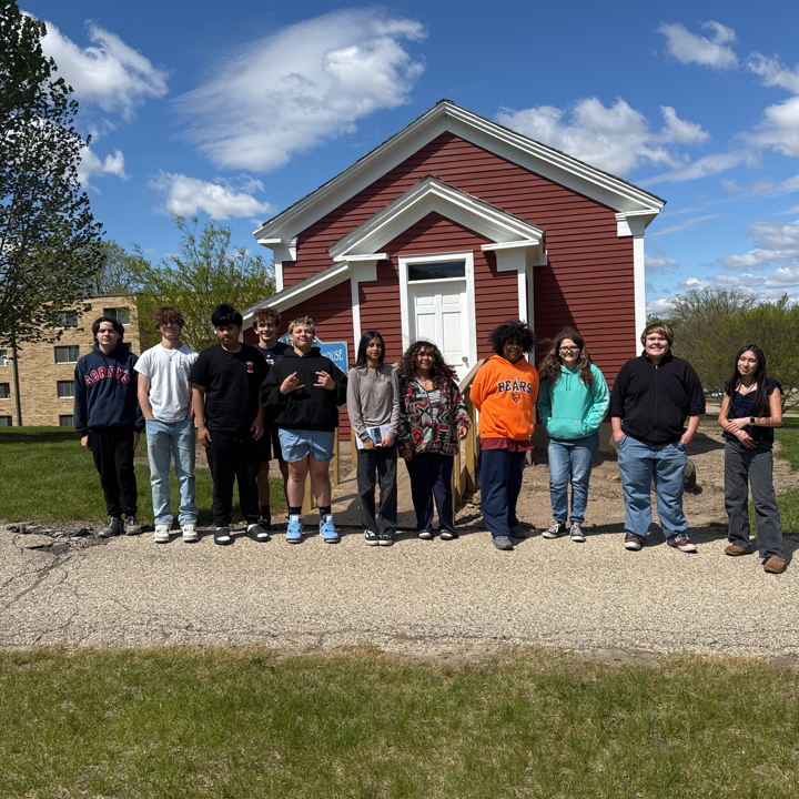 8th graders in front of a small red building