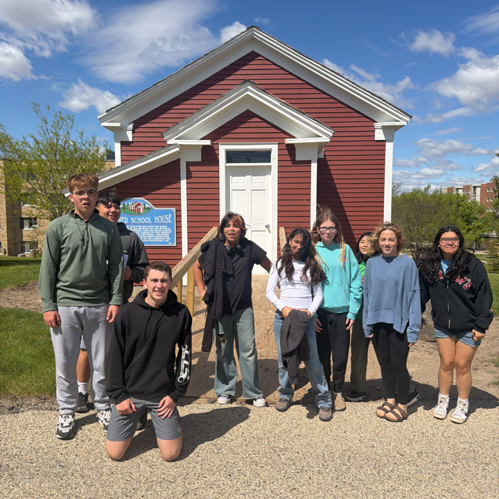 8th grade students in front of a small red building