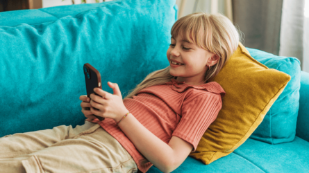 Young girl smiling laying on a couch looking at a smart phone.