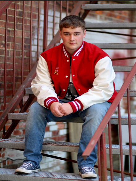 Senior Picture of Tydus Chase sitting on steps in his Youngsville Varsity Jacket