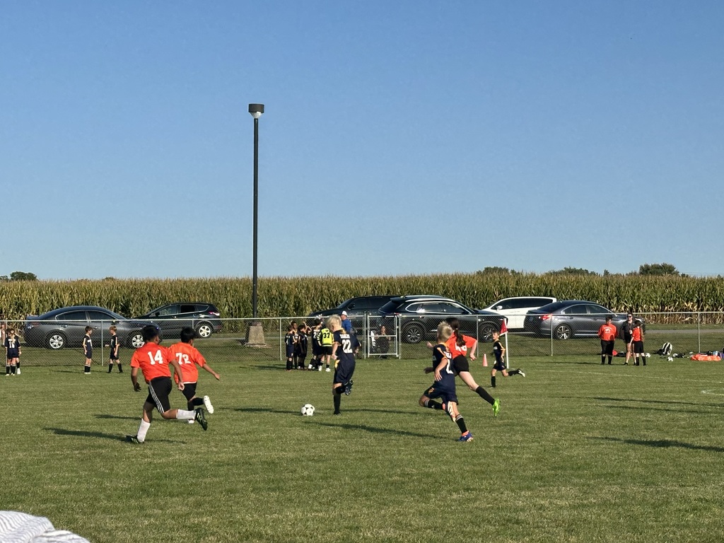 Students playing soccer outside on a green soccer field.