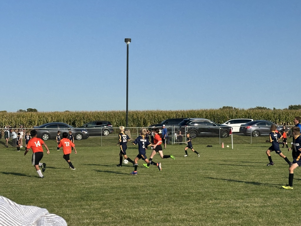 Students playing soccer outside on a green soccer field.
