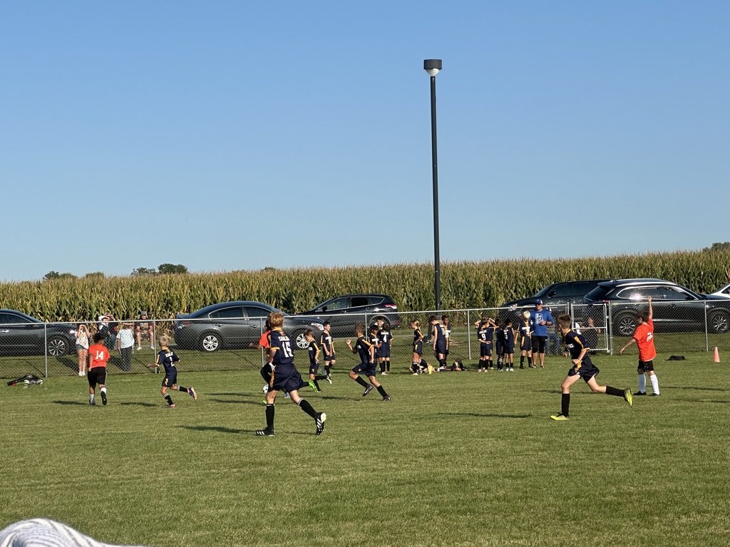 Students playing soccer outside on a green soccer field.