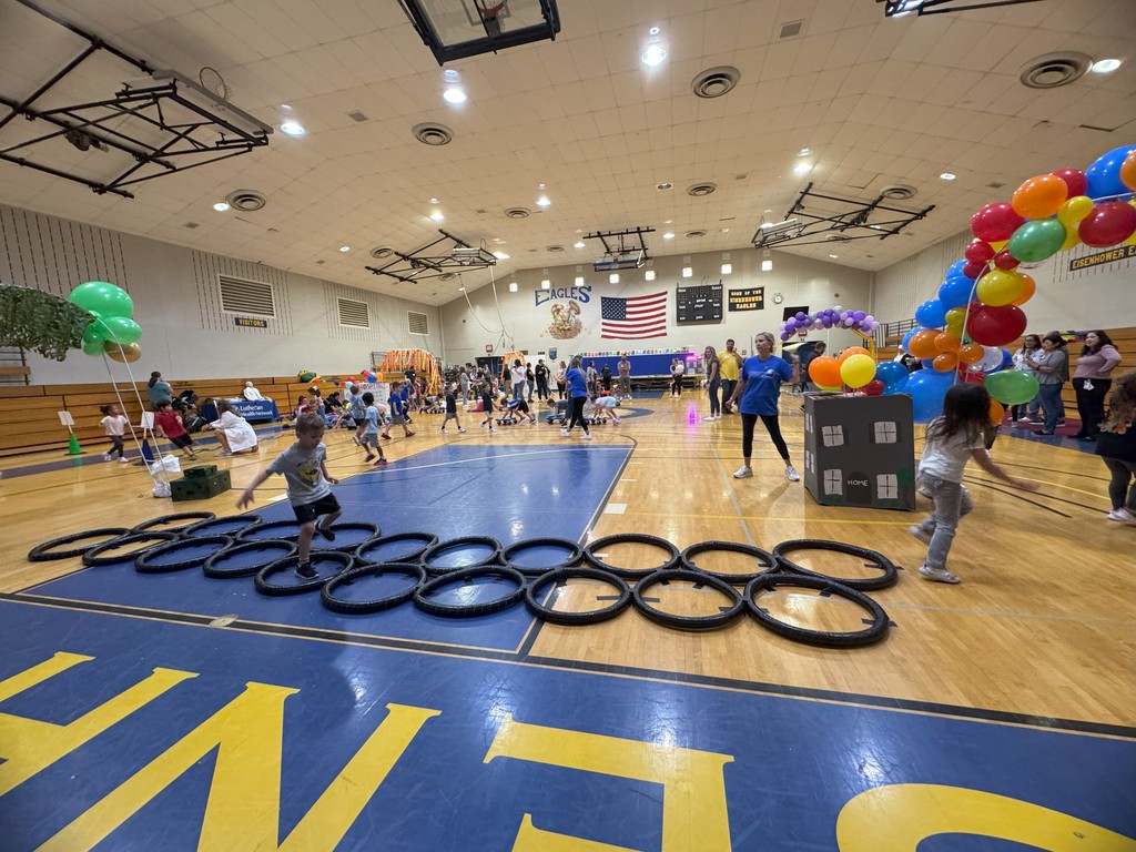 A large indoor gymnasium with a basketball court, colorful balloons, and rubber tires arranged in a pattern on the floor. Banners and signs on the walls.