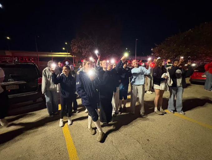 Students gathered together in a parking lot shining lights