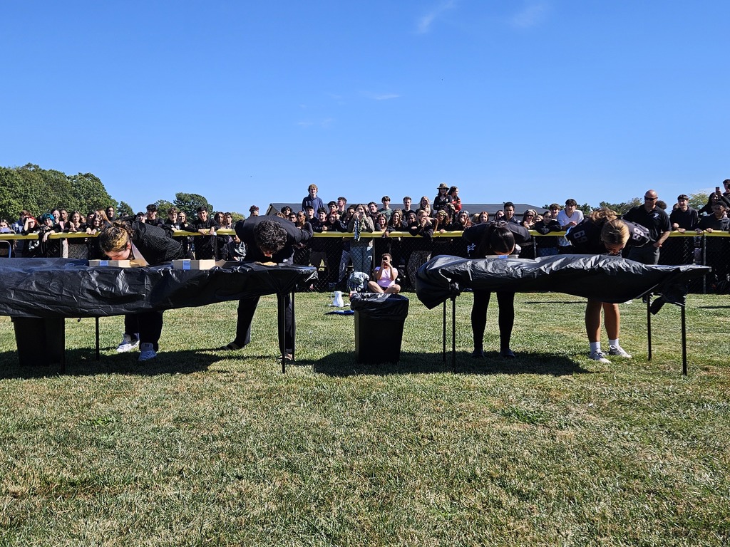 Outside in the softball field with tables and many students