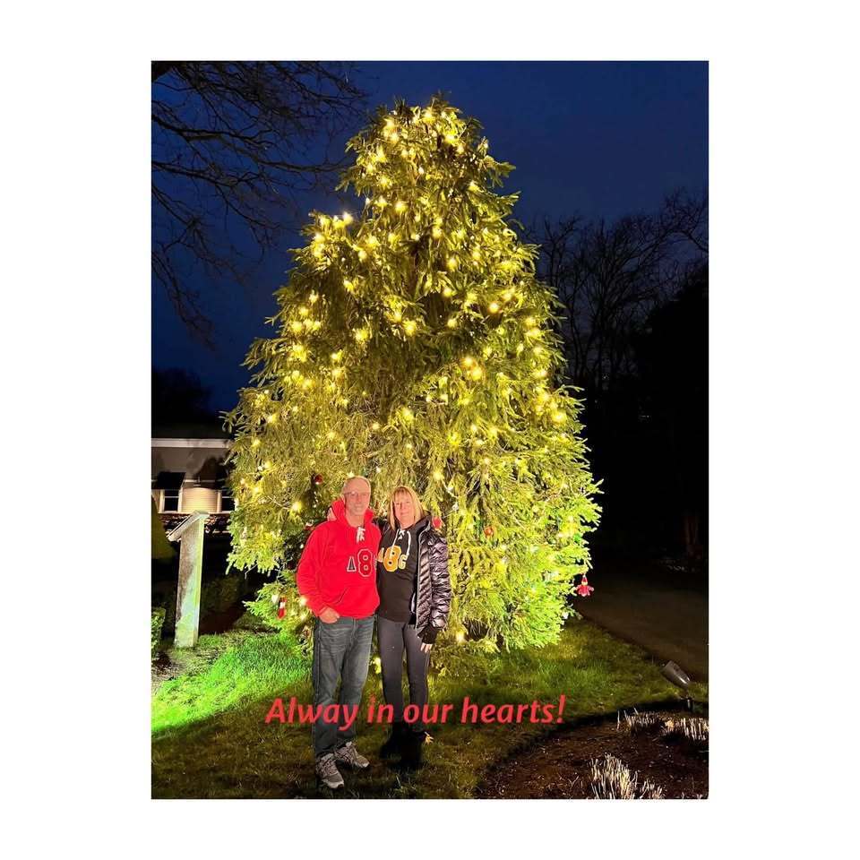 Andrew's parents standing in front of a lit evergreen tree.