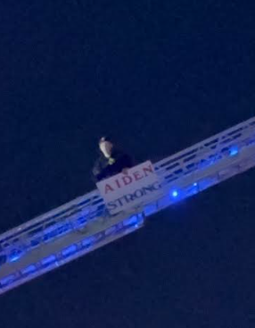 Student on a ladder truck with sign: "Aiden Strong"