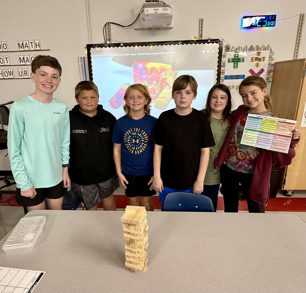 Students pose behind a Jenga tower in a classroom.