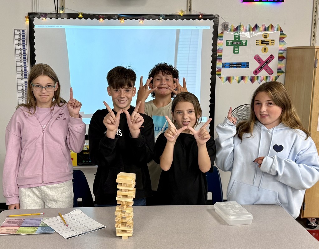 Students pose beside a Jenga tower in a classroom.