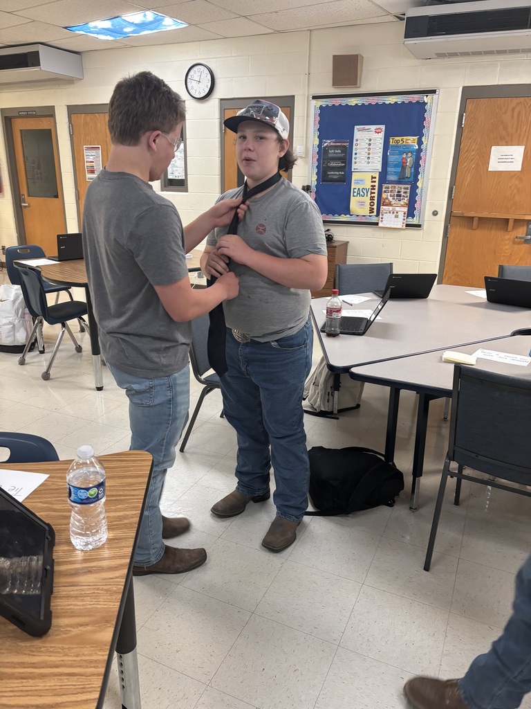 A student shows another student how to tie a tie.