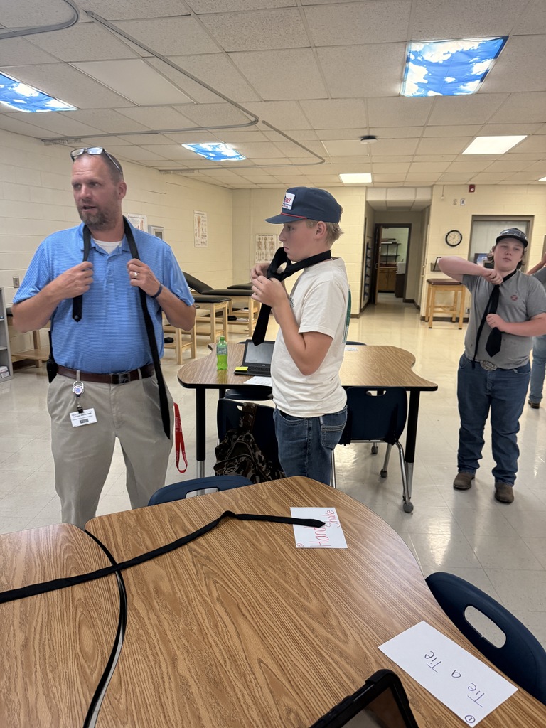 A man shows two students how to tie a tie.