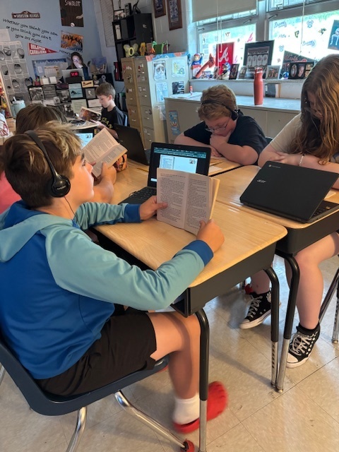 Students read and listen to an audio book in a classroom.