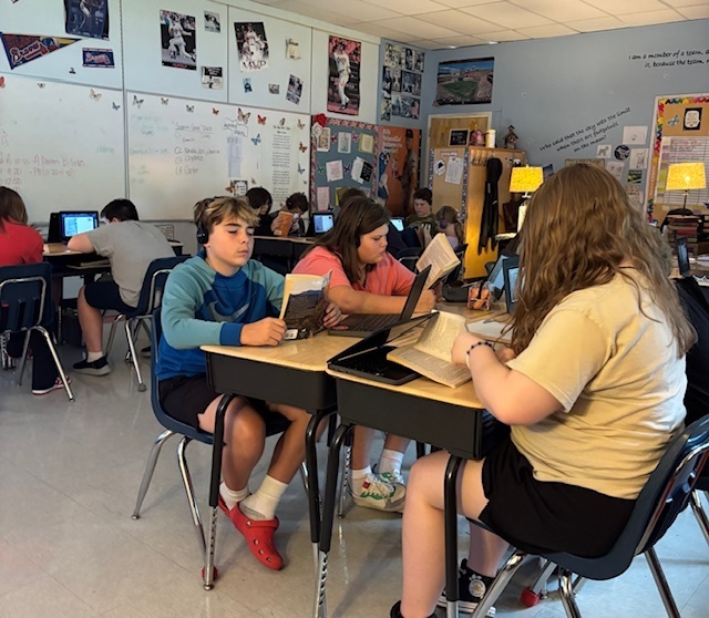 Students read and listen to an audio book in a classroom.