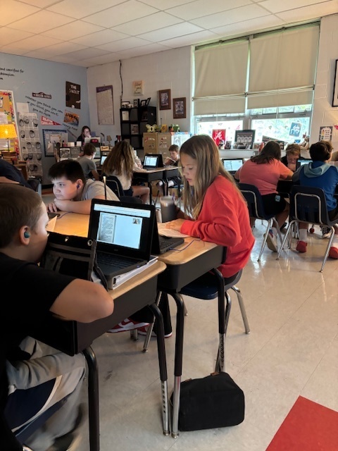 Students read and listen to an audio book in a classroom.